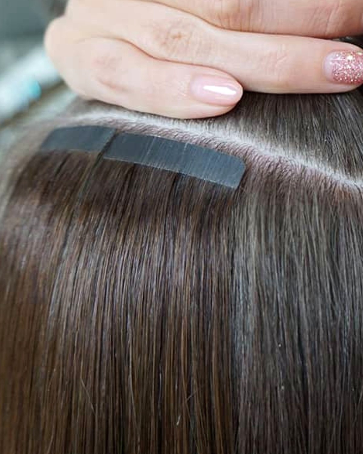 Tape extensions insatta i brunt hår - fästet ligger platt mot hårbotten
